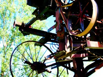 Close-up of Heureka showing rusted gears, wheels, and beams with a yellow belt against green trees and blue sky.
