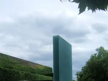 National Police Memorial in London, showing a tall dark teal monolith rising from a rectangular pool beside a smaller dark block and landscaped lawns.