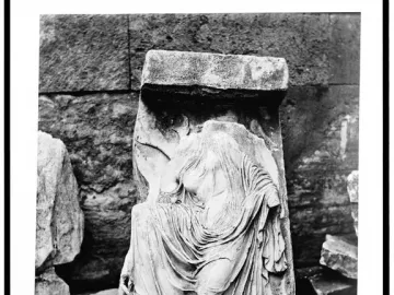 Weathered stone relief of Nike untying her sandal, shown in sepia tones.