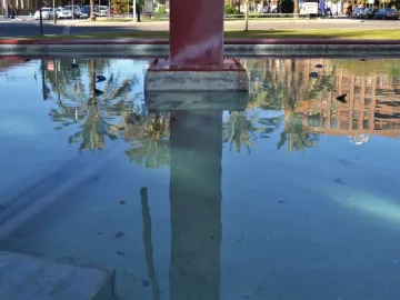 A shallow pool reflecting palm trees and buildings with a reddish-brown Pink Panther sculpture rising from the center.