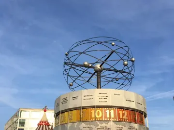 World Clock with an open metal globe on top and city names around the base, with a carousel in the background.