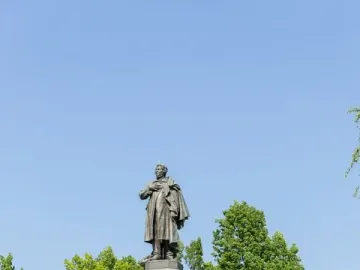 Adam Mickiewicz Monument: a bronze statue of a man in a cloak standing on a tall stone pedestal, with a floral wreath at the base.