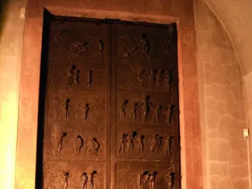 Bernward Doors with bronze relief panels and animal-head door knockers in a stone archway.