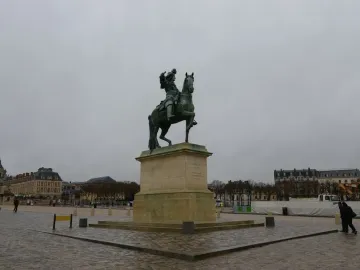 Equestrian Statue of Louis XIV, a green-patinated bronze rider on a rearing horse pointing forward against a blue sky.