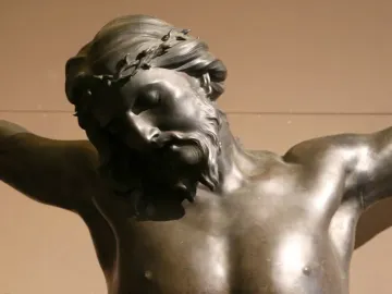 Bronze sculpture of the crucified Christ with bowed head, closed eyes, and outstretched arms.