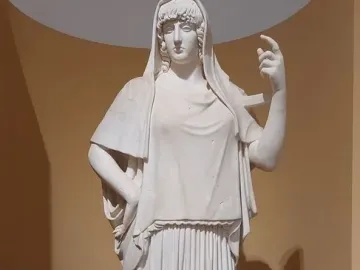 Giustiniani Hestia, a white marble statue of a standing woman in a long pleated robe with a mantle over her head and shoulders.