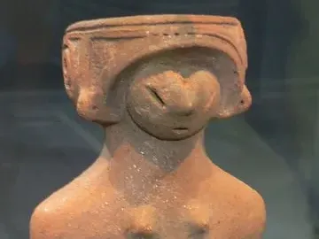 Jōmon Venus clay figurine with a stylized head, prominent breasts, and a rounded lower body on a dark base.