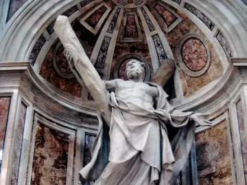 Stone statue of Saint Andrew in a decorated marble alcove, with one arm raised to a wooden beam behind him.