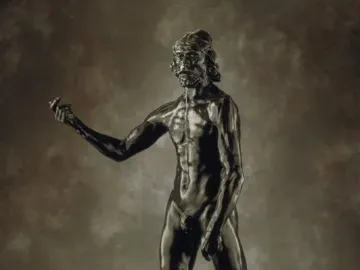 Bronze sculpture of Saint John the Baptist, a muscular bearded male figure standing with one arm outstretched.
