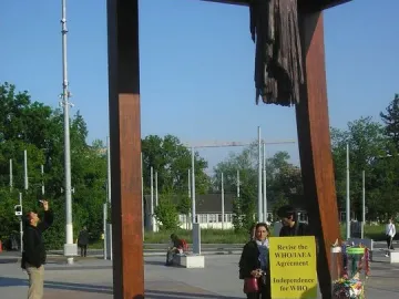 Broken Chair sculpture with one splintered leg hanging from the seat on a paved square.