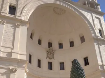 La Pigna pine cone sculpture on an ornate pedestal with peacock statues in front of a curved building facade.