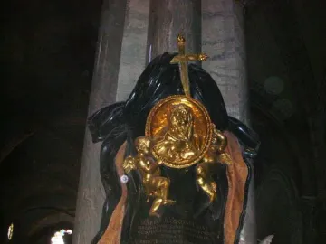 Memorial to Maria Raggi with gilded medallion, putti, and cross on a marble monument in a dim church interior.