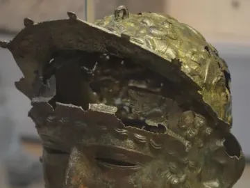 Corroded bronze Ribchester Helmet with a full face mask and damaged upper headpiece.