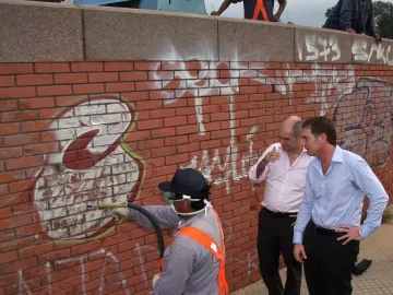 Workers clean graffiti from the Monument to General Carlos M. de Alvear while two men observe nearby.