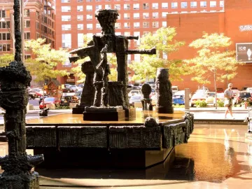 La Joute bronze fountain sculpture with abstract figures and water at its base in an urban plaza.