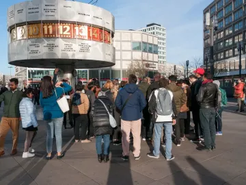 The World Clock stands in a public square with people gathered around its base.