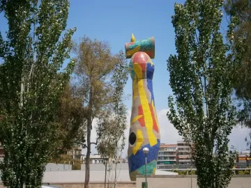 Dona i Ocell sculpture in Barcelona, covered in colorful mosaic tiles with a yellow crescent and ring at the top.