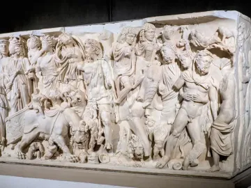 White marble sarcophagus with a densely carved triumphal procession of draped figures and animals in high relief.