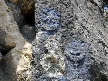 Weathered rock face with ancient carved relief symbols, including circular forms and a radiating star-like motif.