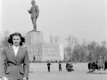 The Stalin Monument rises on a tall pedestal in a large square, with a woman posing in the foreground and people nearby.