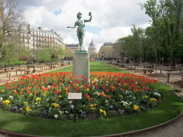 The Greek Actor sculpture on a tall stone pedestal in a flower bed of red and yellow tulips in a Paris park.