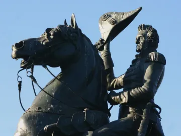 Andrew Jackson equestrian statue in bronze, showing Jackson raising his hat beside the horse’s head against a blue sky.