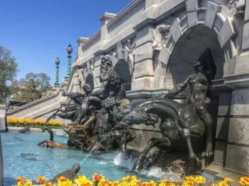 Court of Neptune Fountain with bronze mythological figures and horses spraying water into a turquoise basin, bordered by yellow and red tulips.