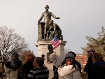 The Emancipation Memorial with Abraham Lincoln standing over a kneeling enslaved man on a stone pedestal, with people gathered around it.