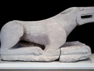 Leona de Baena stone sculpture of a crouching feline beast with its jaws open, displayed on a white base.