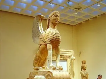 The Sphinx of Naxos statue displayed on a tall column base in a museum hall.