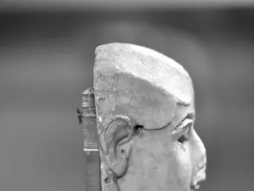 Side profile of the Warka Mask on a dark display stand.