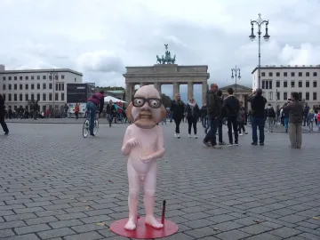 Citizen Włapko sculpture on a red circular base in a square, with the Brandenburg Gate in the background.