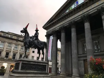 Duke of Wellington equestrian statue with red and white traffic cones on the rider and horse heads, in front of a columned gallery building.