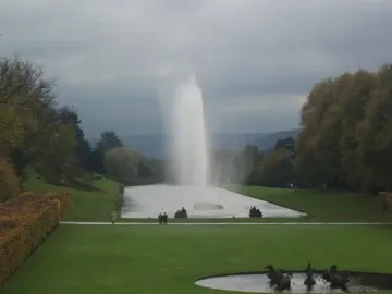The Emperor Fountain sends a tall plume of water over a long lake at Chatsworth, framed by lawns, hedges, and autumn trees.