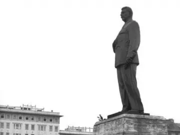 Statue of Joseph Stalin on a stone pedestal, flanked by two armed guards and decorated with flowers.