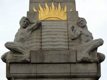 Relief figures on the Titanic Engine Room Heroes Memorial, showing two shirtless male figures beside a central panel with wavy lines and a sunburst above.