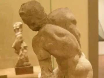 Two Wrestlers sculpture showing two nude male figures locked in a wrestling embrace on a dark base inside a display case.
