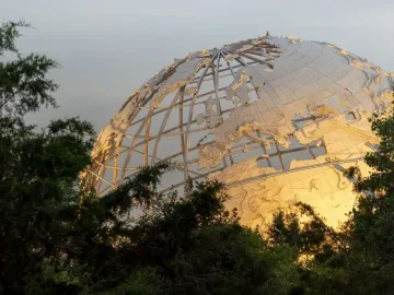 Unisphere partially visible through lush green foliage, with its metallic grid and continental shapes catching warm light.