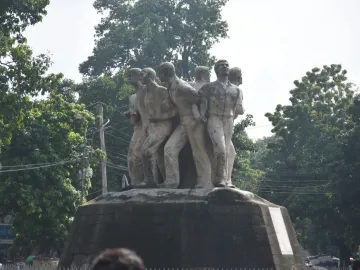 Anti Terrorism Raju Memorial Sculpture with several male figures in forward-moving poses on a dark pedestal, framed by trees.
