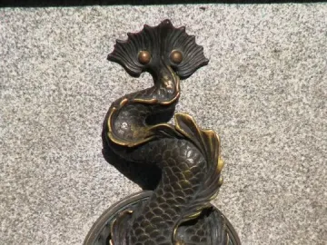 Bronze-colored dragon-shaped fountain spout on the Nicolaus Copernicus Monument, with water flowing from its mouth.