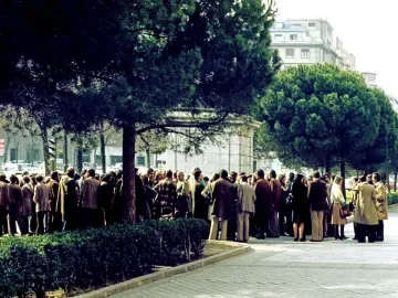 Stone plinth of the Equestrian Statue of Francisco Franco partly hidden by trees, with a crowd gathered around it.