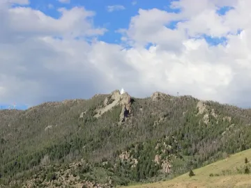 Our Lady of the Rockies statue standing on a rocky, tree-covered mountain summit