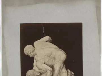 The Wrestlers marble sculpture showing two nude male figures in a wrestling pose on a dark base.