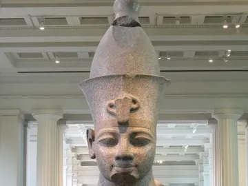 Colossal head of Amenhotep III displayed on a pedestal in a museum gallery.