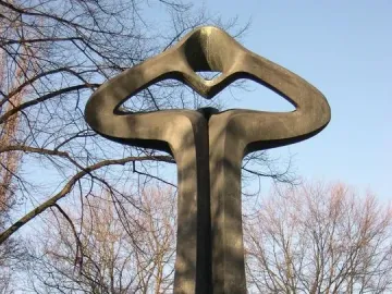 Der Mahner, a tall dark abstract sculpture with a tapering base and open upper form standing on grass.
