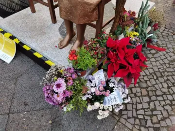 The Peace Statue’s bronze lower legs and bare feet on a stone base, surrounded by floral arrangements and potted plants.