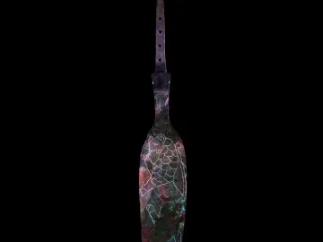 The Spear of Lugal, a weathered dark metal blade with a perforated tang and engraved animal figure against a black background.