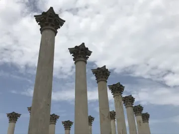 Weathered Capitol Columns stand in a row against a partly cloudy sky.