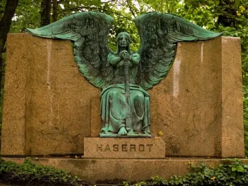Weathered green Haserot Angel statue with large wings mounted on a granite monument.