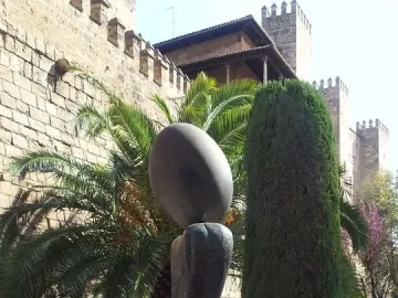 Monument a la dona, a dark abstract sculpture with an oval top on a curved base in an outdoor setting.